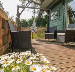 An outdoor deck with wicker chairs daisies and a striped hanging chair at Dart View Hideout in Totnes