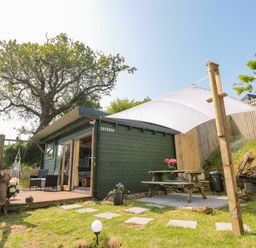 A small green cabin with a wooden deck chairs and a picnic table under a white canopy in a garden at Dart View Hideout in Totnes