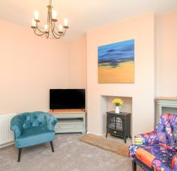 A living room with a blue armchair a floral armchair a black stove a television on a stand and a painting above the stove at The Skipper's House in Weymouth