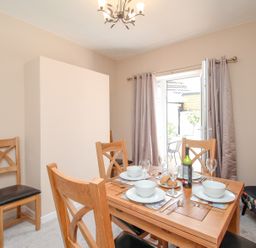 A dining room with a wooden table set for four and chairs with cushions next to curtains and glass doors at The Skipper's House in Weymouth
