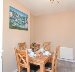 A dining room with a wooden table set for four with white bowls wine glasses and cutlery a painting on the wall and a radiator at The Skippers House in Weymouth