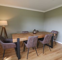 A dining room with a wooden table six chairs a floor lamp and a vase on the table at Sea View in St Clears