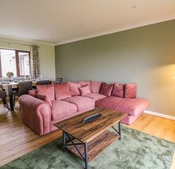 A living room with a pink sectional sofa and wooden coffee table next to a dining area with a table and chairs at The Oaks in St Clears