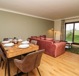 A dining table set with plates and glasses next to a pink sofa and a coffee table in a room with sliding glass door at The Oaks in St Clears