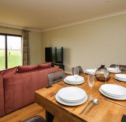 A dining table set with plates glasses and cutlery next to a living room with a red sofa and television at The Oaks in St Clears