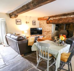 A living room with a brown leather sofa a dining table with two chairs a wood burning stove and a television at The Bake House in Bettws