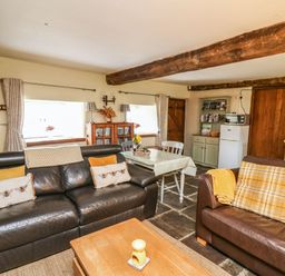 A living room with two leather sofas a wooden coffee table and a dining table with chairs at The Bake House in Bettws