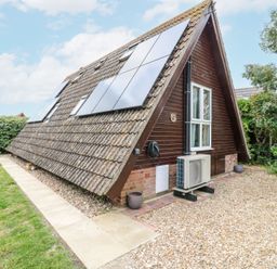 An A-frame house with solar panels on the roof a paved walkway grassy area and gravel driveway at Kingfisher in Isleham
