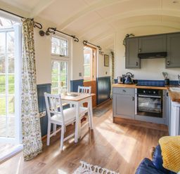 A kitchen area with grey cabinets white dining table and chairs wooden countertops and open doors to outside at Mucklewick Hollow in Minsterley near Bishops Castle
