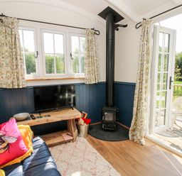 A living room with a blue sofa a wooden TV stand a black wood stove and open glass doors leading to a patio at Mucklewick Hollow in Minsterley near Bishops Castle