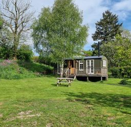 A small house with a wooden porch surrounded by trees and grass with a picnic table on the lawn at Mucklewick Hollow in Minsterley near Bishops Castle
