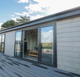 Sliding glass doors open to a living room with a wooden coffee table on a deck outside at Bluebell Lodge in Norton near Dartmouth