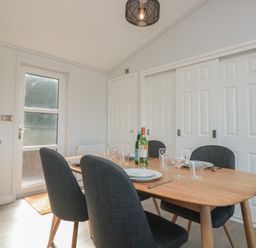 A dining area with a wooden table set with plates glasses and bottles and four dark upholstered chairs at Bluebell Lodge in Norton near Dartmouth