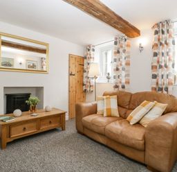 A living room with a brown leather sofa a wooden coffee table a floor lamp patterned curtains and a wall mirror at 4 Wallflower Row in Mordiford near Hereford