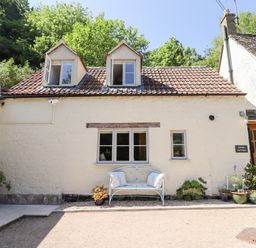 Exterior of a cottage with two dormer windows a bench and potted plants at Spring Cottage in Stroud