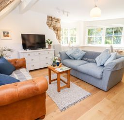 A living room with two sofas a wooden coffee table a white TV stand with a television and large windows at Spring Cottage in Stroud
