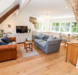 A living room with sofas a wooden coffee table a television and large windows at Spring Cottage in Stroud