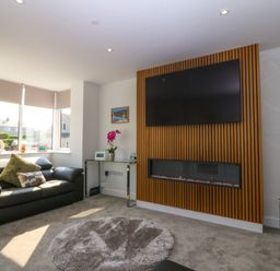 A living room with a black sofa a round rug a wall-mounted TV and a fireplace at Hedd in Amlwch