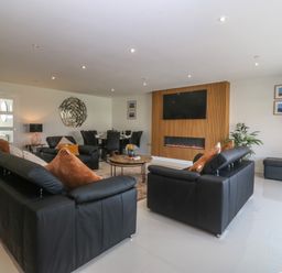 A living room with black leather sofas and a wall-mounted television above a fireplace at Hedd in Amlwch