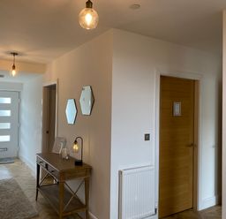 An entrance hallway with a wooden console table two hexagonal mirrors rugs wooden doors and hanging light fixtures at Galwad y Mor in Broad Haven