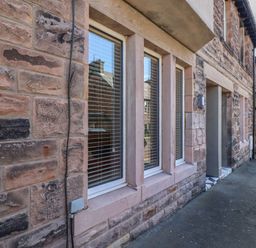 Stone exterior wall with three windows and a doorway along a paved street at Glencoe House in Wooler