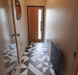 A hallway with geometric patterned floor tiles a wooden front door a black radiator and a round mirror at Glencoe House in Wooler