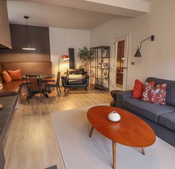 A living room with a gray sofa red cushions a wooden coffee table and a dining area with brown seating at Glencoe House in Wooler