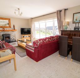 A living room with a stone fireplace a television red sofas a wooden piano and large windows at Inverbeg Cottage 1 in Downings