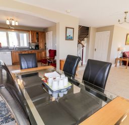 A dining area with a glass table and black chairs next to a kitchen with wooden cabinets and a living room with red sofas at Inverbeg Cottage 1 in Downings