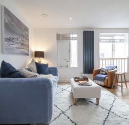 A living room with a blue sofa brown armchair white rug and coffee table at The Gallivant in Southwold