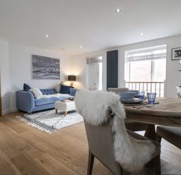 A living room with a blue sofa a wooden dining table and chairs and a window at The Gallivant in Southwold