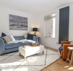 A living room with a blue sofa white ottoman wooden side table and a brown armchair at The Gallivant in Southwold