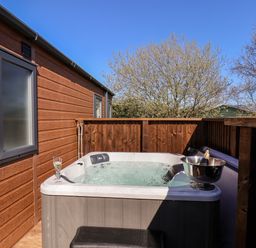 An outdoor hot tub with bubbling water next to a wooden building and a wooden fence with a bottle and glass on the tub at Mayflower Lodge in Runswick Bay near Staithes
