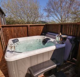 An outdoor hot tub with two glasses of champagne and a bottle in an ice bucket on a fenced wooden deck at Foxglove Lodge Runswick Bay near Staithes