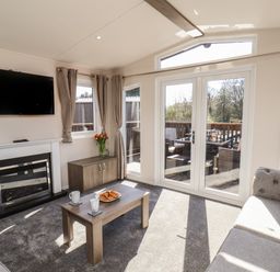 A living room with a fireplace a wall mounted television two sofas a coffee table and glass doors leading to a deck at Foxglove Lodge in Runswick Bay near Staithes