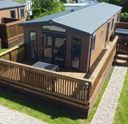 A wooden cabin with a fenced deck and stone path on grass at Foxglove Lodge in Runswick Bay near Staithes