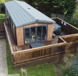 A wooden cabin with a gray metal roof and a fenced wooden deck in a grassy area at Tulip Lodge in Runswick Bay near Staithes