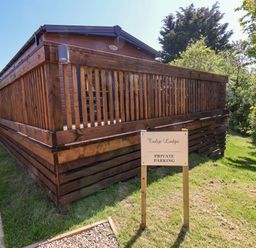 A wooden lodge with a fenced deck and a sign indicating private parking on grass at Tulip Lodge Runswick Bay near Staithes