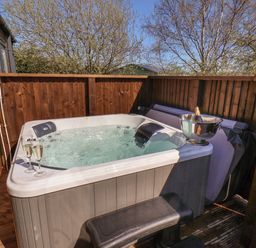 An outdoor hot tub with two glasses of champagne and a champagne bottle in an ice bucket on a wooden deck at Buttercup Lodge in Runswick Bay near Staithes