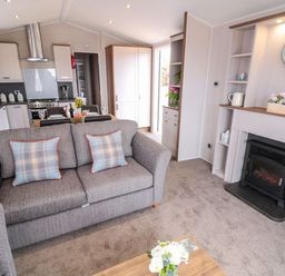 A living room with a sofa dining table kitchen and fireplace at Rose Lodge in Runswick Bay near Staithes