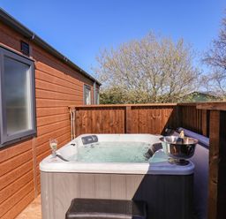 An outdoor hot tub with a glass of drink and a bottle in an ice bucket on a wooden deck at Honeysuckle Lodge in Runswick Bay near Staithes