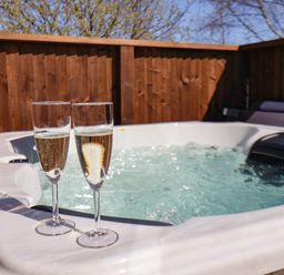A hot tub with two glasses of sparkling wine on the ledge and a wooden fence in the background at Honeysuckle Lodge in Runswick Bay near Staithes