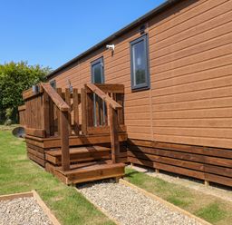 An exterior view of a wooden cabin with small steps and a gravel path outside at Honeysuckle Lodge in Runswick Bay near Staithes