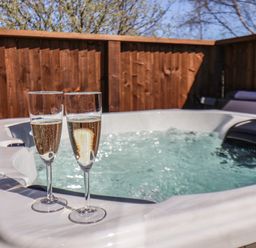 Two glasses of champagne on the edge of a bubbling hot tub with wooden fencing and trees in the background at Lilac Lodge in Runswick Bay near Staithes