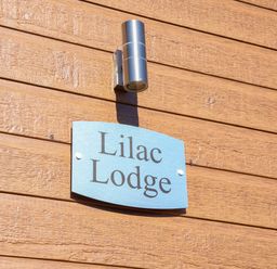 A blue sign with Lilac Lodge on a wooden wall under a metal light at Lilac Lodge in Runswick Bay near Staithes