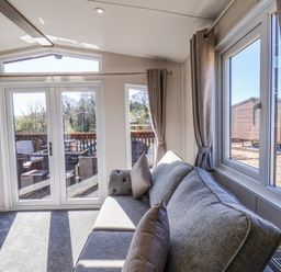 A living room with a gray sofa and large windows showing a deck with outdoor furniture at Lilac Lodge in Runswick Bay near Staithes