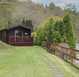 A wooden cabin with a small porch surrounded by grass trees and a wooden fence at Canadian Cabin 37 in Keswick