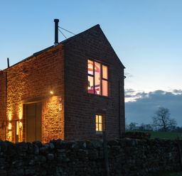 A stone house illuminated at dusk with a stone wall in front and fields in the background at Shepherds View in Dufton near Appleby-in-Westmorland