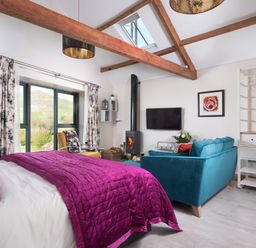 A bedroom with a bed purple blanket teal sofa yellow chair wood stove and window at Shepherds View Dufton near Appleby-in-Westmorland