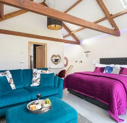 A bedroom with a purple bed, teal sofa, wooden beams on ceiling, and a tray with snacks at Shepherds View in Dufton near Appleby-in-Westmorland